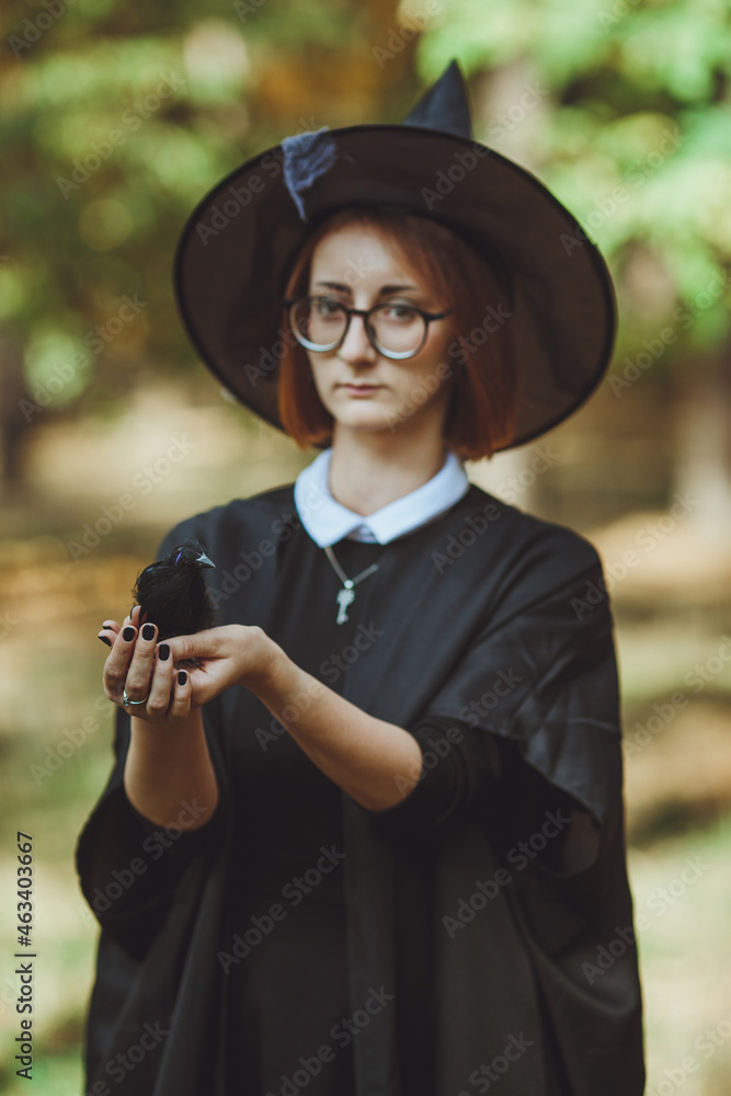 Halloween witch. Portrait of a girl in a hat and witch costume and with a black raven in the forest. Ready for the holiday wallet or life