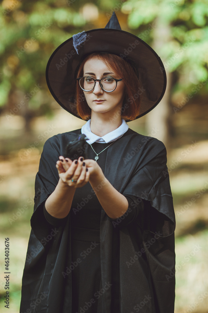 Halloween witch. Portrait of a girl in a hat and witch costume and with a black raven in the forest. Ready for the holiday wallet or life