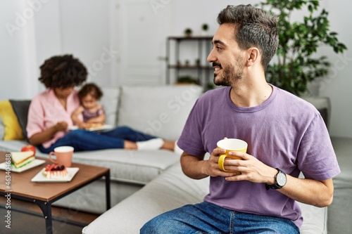 Hispanic father of interracial family drinking a cup coffee looking to side  relax profile pose with natural face and confident smile.