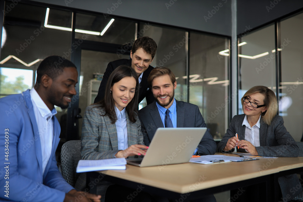 Group of happy diverse male and female business people in formal gathered around laptop computer in bright office.