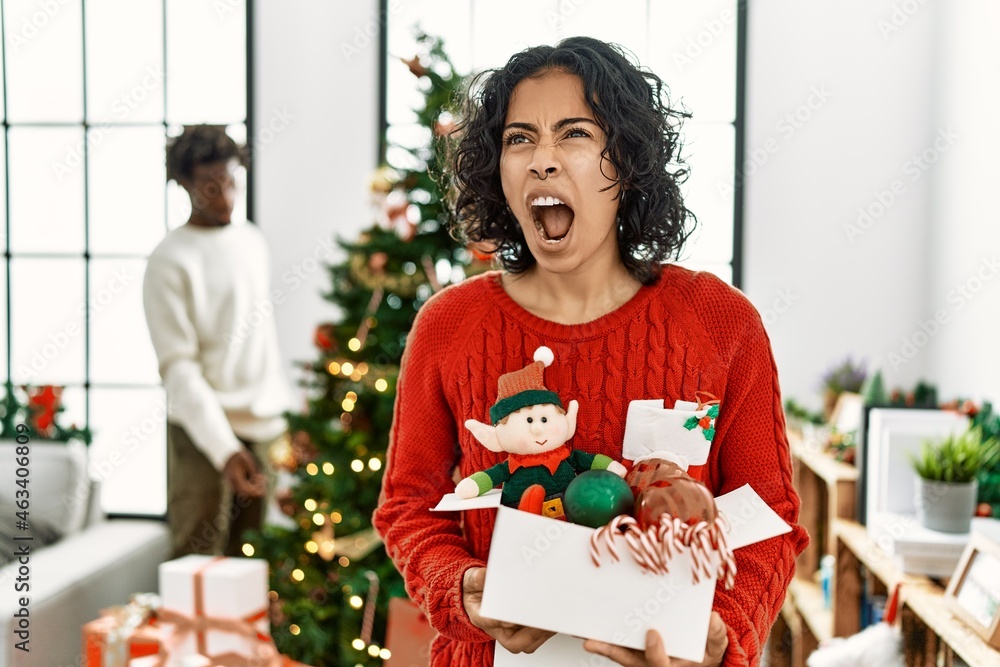 Young hispanic woman standing by christmas tree with decoration angry and mad screaming frustrated and furious, shouting with anger. rage and aggressive concept. Young hispanic woman standing by christmas tree with decoration angry and mad screaming frustrated and furious, shouting with anger. rage and aggressive concept.