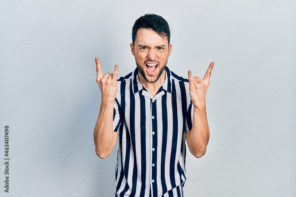 Young hispanic man wearing casual clothes shouting with crazy expression doing rock symbol with hands up. music star. heavy concept. Young hispanic man wearing casual clothes shouting with crazy expression doing rock symbol with hands up. music star. heavy concept.