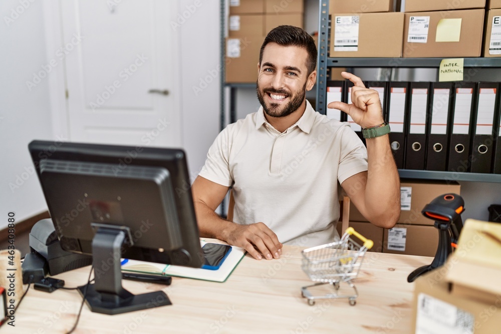 Handsome hispanic man working at small business commerce smiling and confident gesturing with hand doing small size sign with fingers looking and the camera. measure concept. Handsome hispanic man working at small business commerce smiling and confident gesturing with hand doing small size sign with fingers looking and the camera. measure concept.