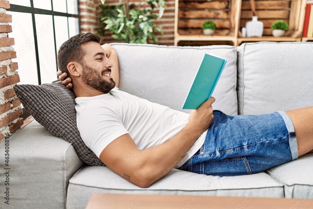 Young hispanic man smiling confident reading book at home