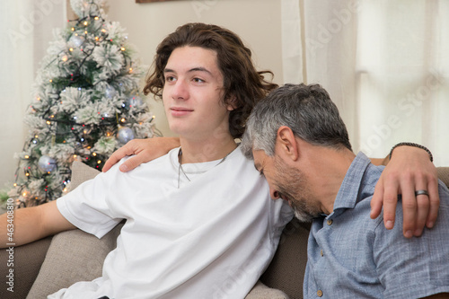 un père de famille fait un câlin à son fils et met la tête sur son épaule le jour de noël, ils sont heureux © Tof - Photographie