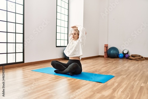 Young blonde girl concentrated stretching at sport center.