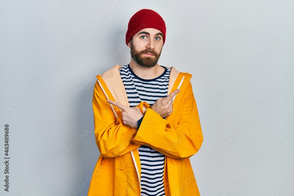 Caucasian man with beard wearing yellow raincoat pointing to both sides with fingers, different direction disagree