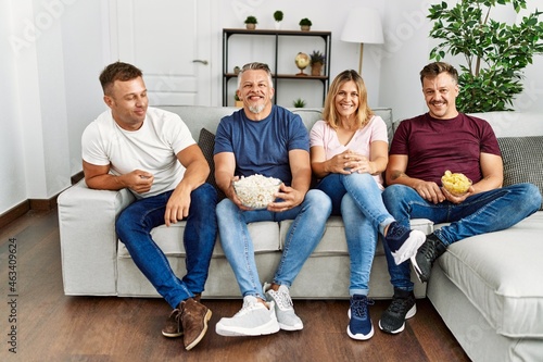 Group of middle age caucasian friends smiling happy watching movie at home.