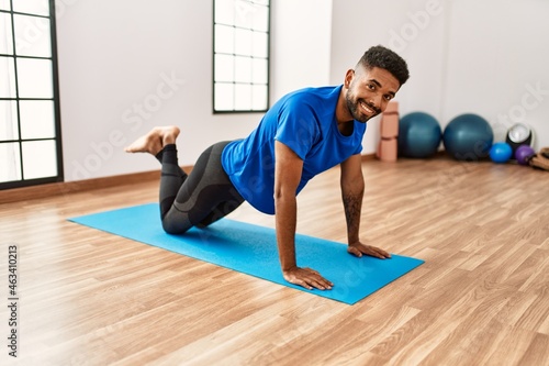 Handsome hispanic man doing exercise and stretching on yoga mat, practicing flexibility and training at the gym