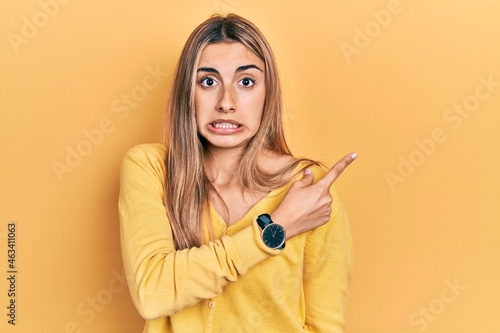 Beautiful hispanic woman wearing casual yellow sweater pointing aside worried and nervous with forefinger, concerned and surprised expression