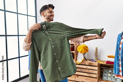 Fotografía Handsome hispanic man shopping trying on a shirt at retail shop