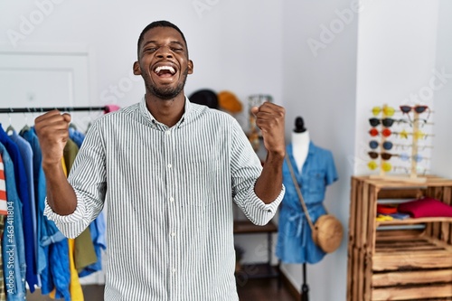 Young african american man working as manager at retail boutique celebrating surprised and amazed for success with arms raised and open eyes. winner concept.