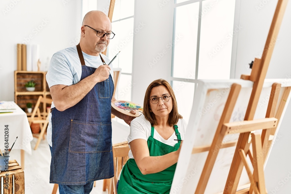 Middle age hispanic painter couple with serious expression painting at art studio. Middle age hispanic painter couple with serious expression painting at art studio.