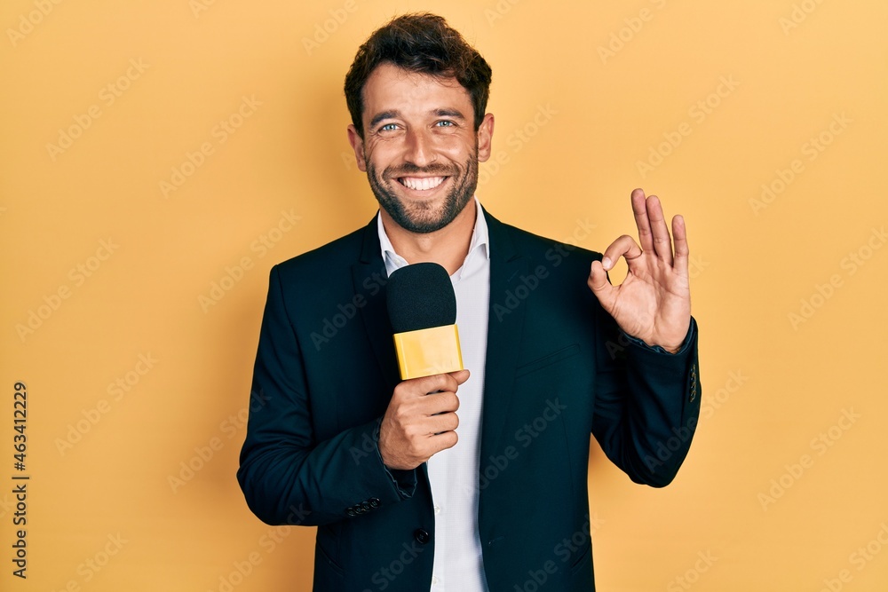 Handsome man with beard holding reporter microphone doing ok sign with fingers, smiling friendly gesturing excellent symbol Handsome man with beard holding reporter microphone doing ok sign with fingers, smiling friendly gesturing excellent symbol