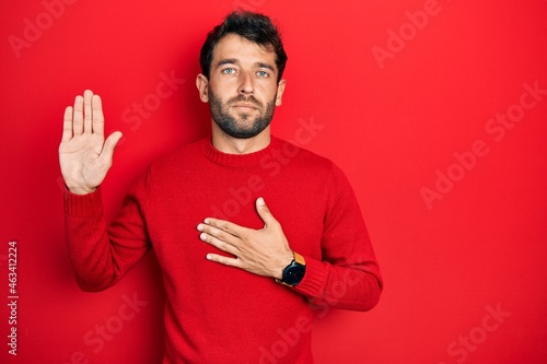 Handsome man with beard wearing casual red sweater swearing with hand on chest and open palm, making a loyalty promise oath