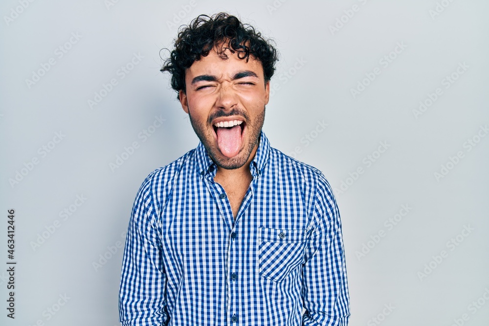 Obraz premium Young hispanic man wearing casual clothes sticking tongue out happy with funny expression. emotion concept.