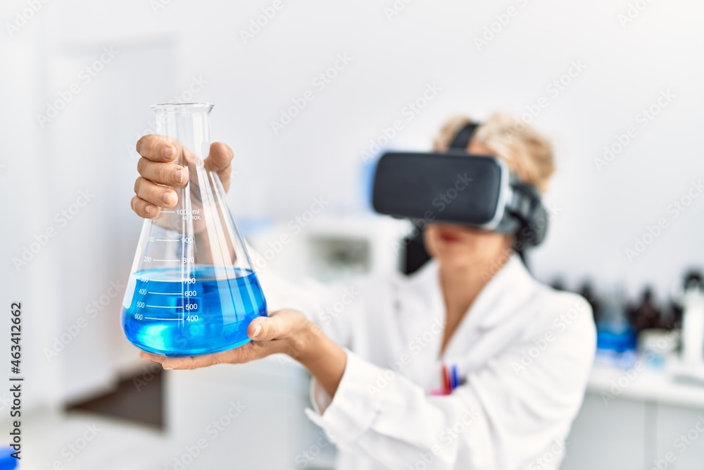 Middle age blonde woman wearing scientist uniform using vr goggles holding test tube at laboratory Middle age blonde woman wearing scientist uniform using vr goggles holding test tube at laboratory