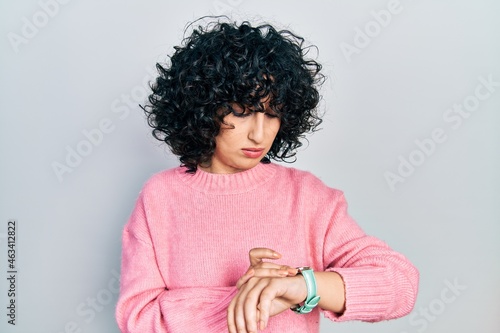 Young middle east woman wearing casual clothes checking the time on wrist watch, relaxed and confident