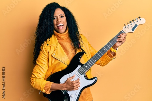 Middle age african american woman playing electric guitar smiling and laughing hard out loud because funny crazy joke.