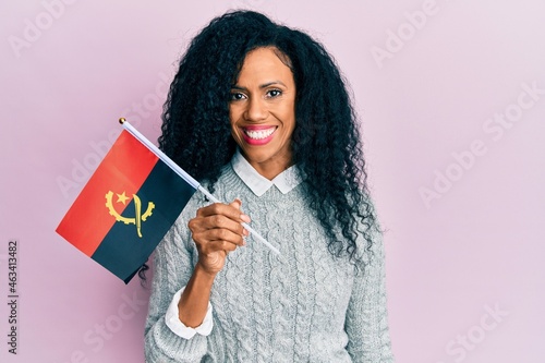Middle age african american woman holding angola flag looking positive and happy standing and smiling with a confident smile showing teeth photo