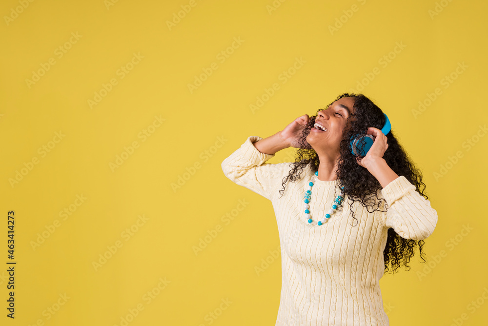 Mujer morena afroamericana escuchando musica con auriculares en fondo amarillo Mujer morena afroamericana escuchando musica con auriculares en fondo amarillo