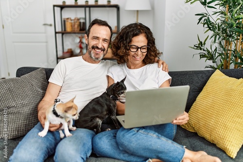 Middle age hispanic couple smiling happy and using laptop. Sitting on the sofa with dogs at home. © Krakenimages.com
