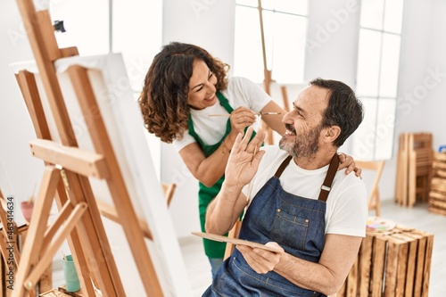 Two middle age students smiling happy playing with paintbrush painting to each other at art school.