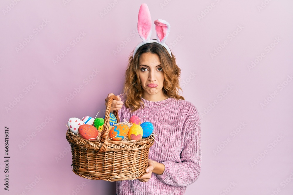 Young caucasian woman wearing cute easter bunny ears holding colored egg depressed and worry for distress, crying angry and afraid. sad expression.