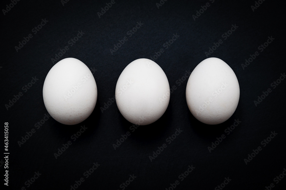 Breakfast triple: three white chicken eggs against a dark slate background. Table top view, flat lay, copy space. Breakfast triple: three white chicken eggs against a dark slate background. Table top view, flat lay, copy space.