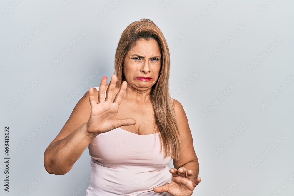 Middle age hispanic woman wearing casual style with sleeveless shirt disgusted expression, displeased and fearful doing disgust face because aversion reaction. with hands raised Middle age hispanic woman wearing casual style with sleeveless shirt disgusted expression, displeased and fearful doing disgust face because aversion reaction. with hands raised