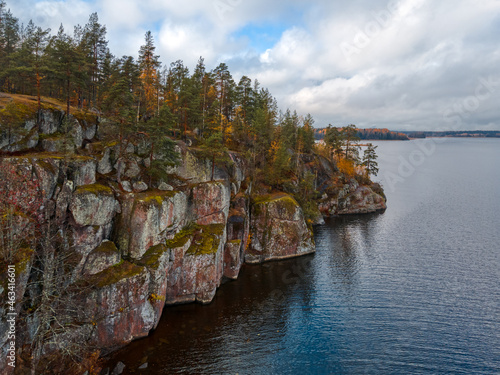 Aerial view of rocky shore with evergreen trees and plants, lake and cloudy sky. Scandinavian nature, skerries and fjords. Autumn season. Beauty in nature. Pure environment. Viborg, Russia.