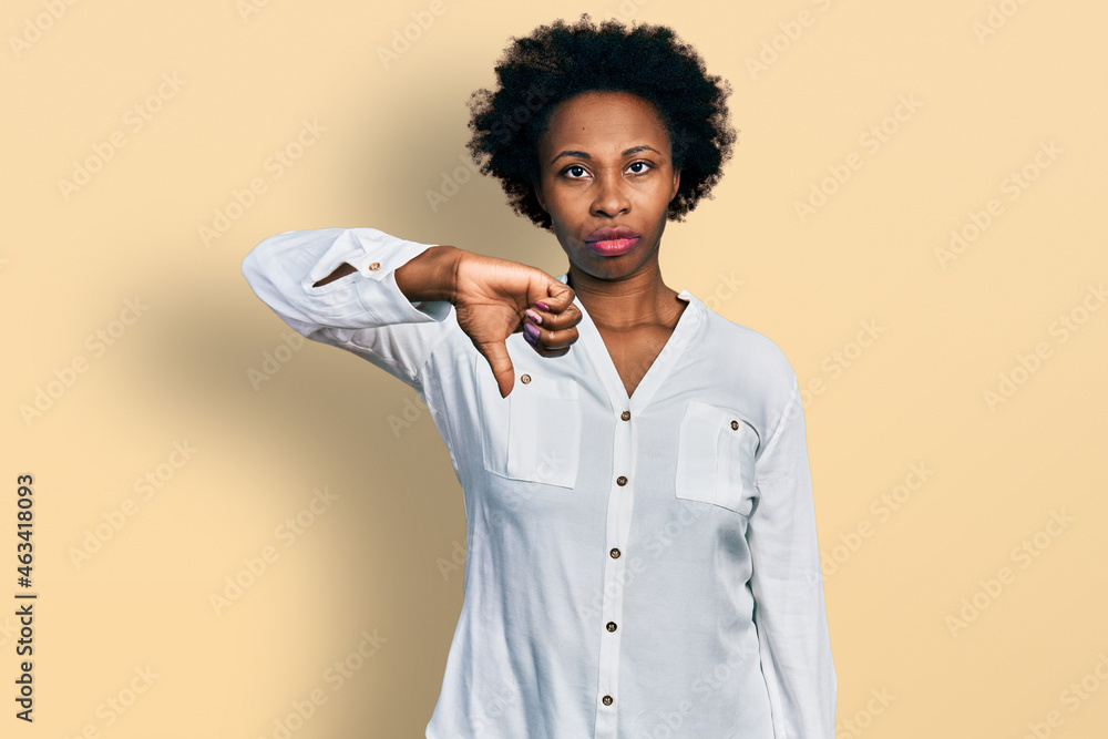 African american woman with afro hair wearing casual white t shirt looking unhappy and angry showing rejection and negative with thumbs down gesture. bad expression. African american woman with afro hair wearing casual white t shirt looking unhappy and angry showing rejection and negative with thumbs down gesture. bad expression.