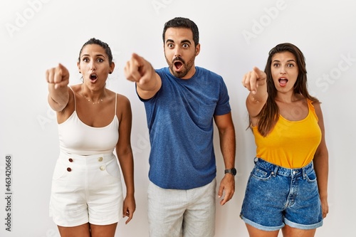 Group of young hispanic people standing over isolated background pointing with finger surprised ahead  open mouth amazed expression  something on the front