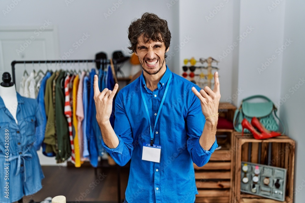 Young hispanic man working as manager at retail boutique shouting with crazy expression doing rock symbol with hands up. music star. heavy concept. Young hispanic man working as manager at retail boutique shouting with crazy expression doing rock symbol with hands up. music star. heavy concept.