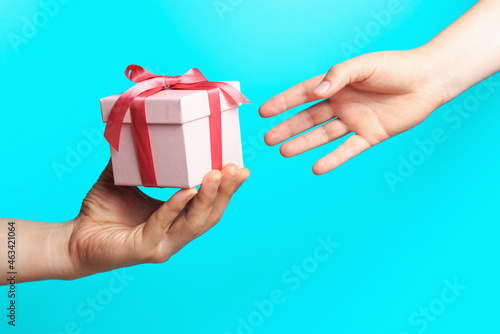 Fototapeta Naklejka Na Ścianę i Meble -  Male hand giving a gift box to female hand on blue background.