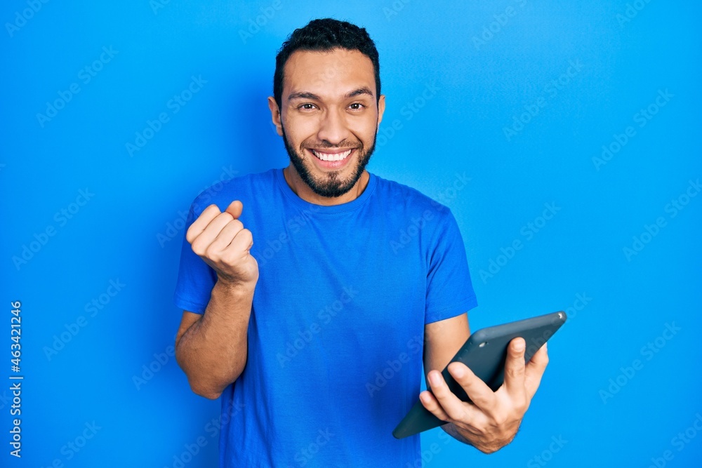 Hispanic man with beard using touchpad device screaming proud, celebrating victory and success very excited with raised arm Hispanic man with beard using touchpad device screaming proud, celebrating victory and success very excited with raised arm