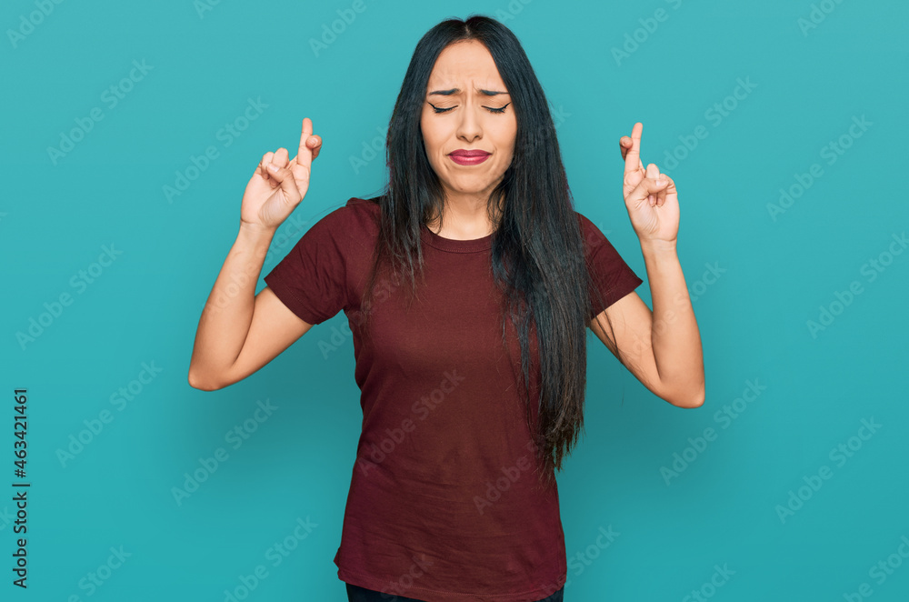 Young hispanic girl wearing casual t shirt gesturing finger crossed smiling with hope and eyes closed. luck and superstitious concept. Young hispanic girl wearing casual t shirt gesturing finger crossed smiling with hope and eyes closed. luck and superstitious concept.