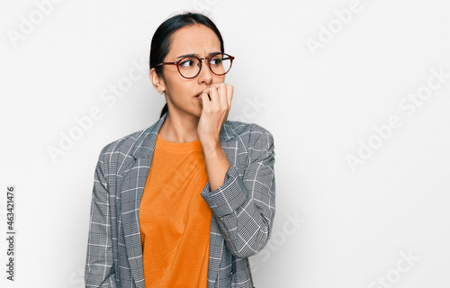 Young hispanic girl wearing business jacket and glasses looking stressed and nervous with hands on mouth biting nails. anxiety problem.