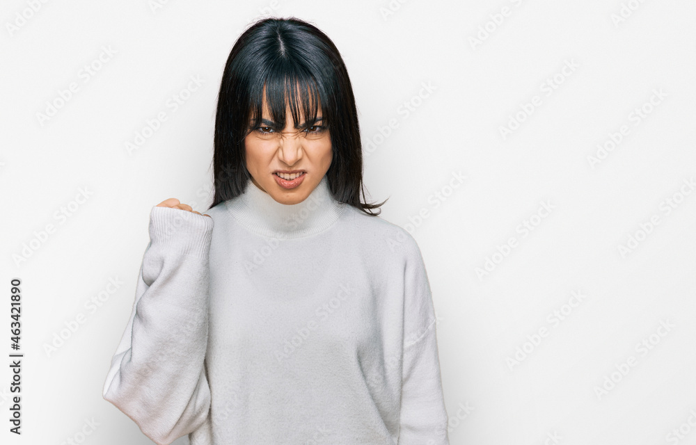Young brunette woman with bangs wearing casual turtleneck sweater angry and mad raising fist frustrated and furious while shouting with anger. rage and aggressive concept. Young brunette woman with bangs wearing casual turtleneck sweater angry and mad raising fist frustrated and furious while shouting with anger. rage and aggressive concept.