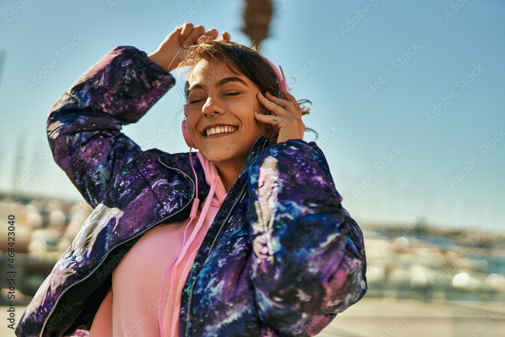 Young hispanic sporty woman smiling happy using headphones dancing at the city.