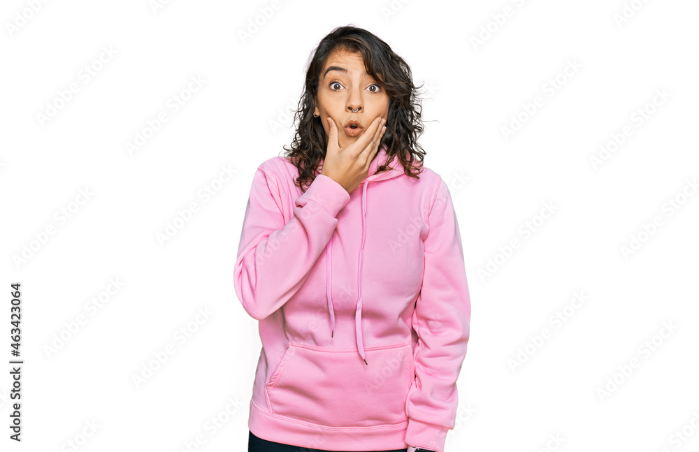 Young hispanic woman wearing casual sweatshirt looking fascinated with disbelief, surprise and amazed expression with hands on chin Young hispanic woman wearing casual sweatshirt looking fascinated with disbelief, surprise and amazed expression with hands on chin