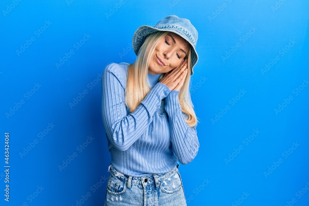 Young blonde woman wearing casual denim hat sleeping tired dreaming and posing with hands together while smiling with closed eyes. Young blonde woman wearing casual denim hat sleeping tired dreaming and posing with hands together while smiling with closed eyes.