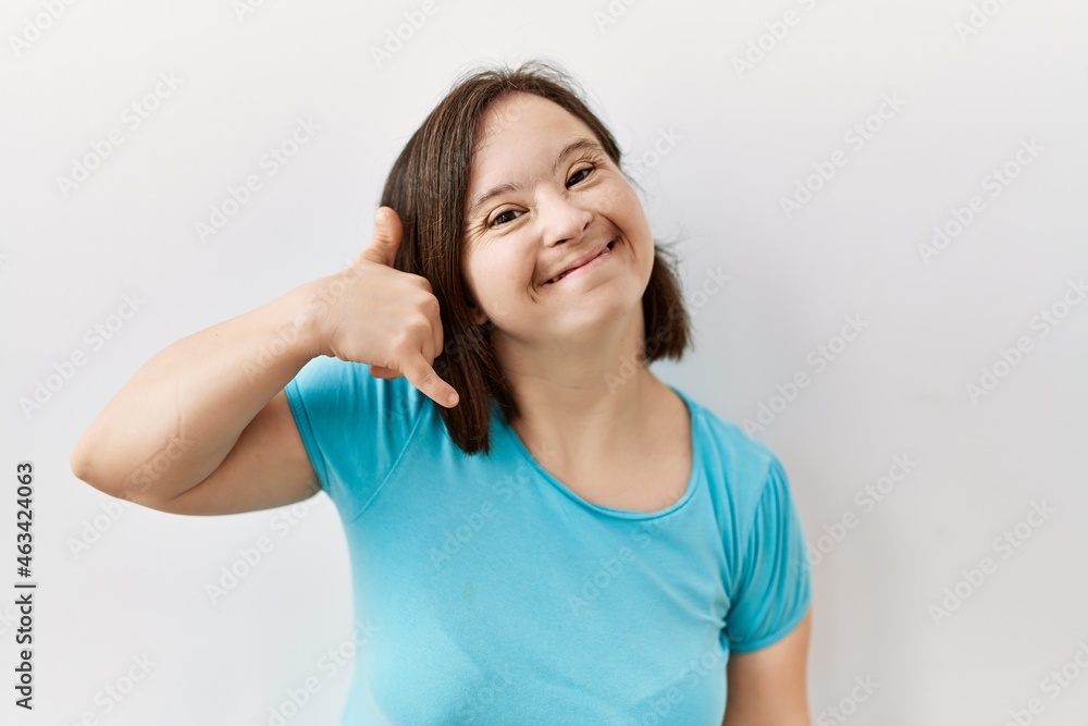 Young down syndrome woman standing over isolated background smiling doing phone gesture with hand and fingers like talking on the telephone. communicating concepts. Young down syndrome woman standing over isolated background smiling doing phone gesture with hand and fingers like talking on the telephone. communicating concepts.