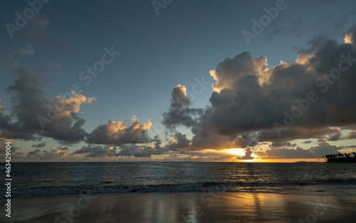 beach vacation sunset scenic suns sunrise reflection on the wet sand from waves receding Caribbean sea waves in the Dominican Republic sun setting behind clouds with golden glow in sky horizontal 