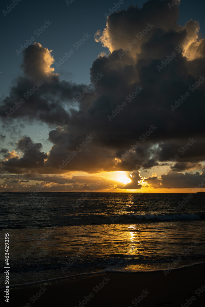 beach vacation sunset scenic suns sunrise reflection on the wet sand from waves receding Caribbean sea waves in the Dominican Republic sun setting behind clouds with golden glow in sky vertical