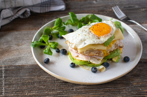 Keto breakfast sandwich with fried eggs, ham, cheese, and avocado. Served with fresh blueberries and lamb´s lettuce