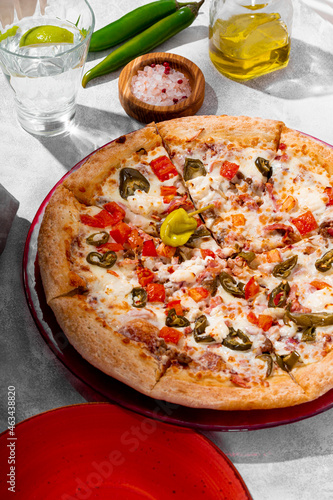 Spicy pizza with chicken, tomatoes and jalapenos on the light gray table vertical photo