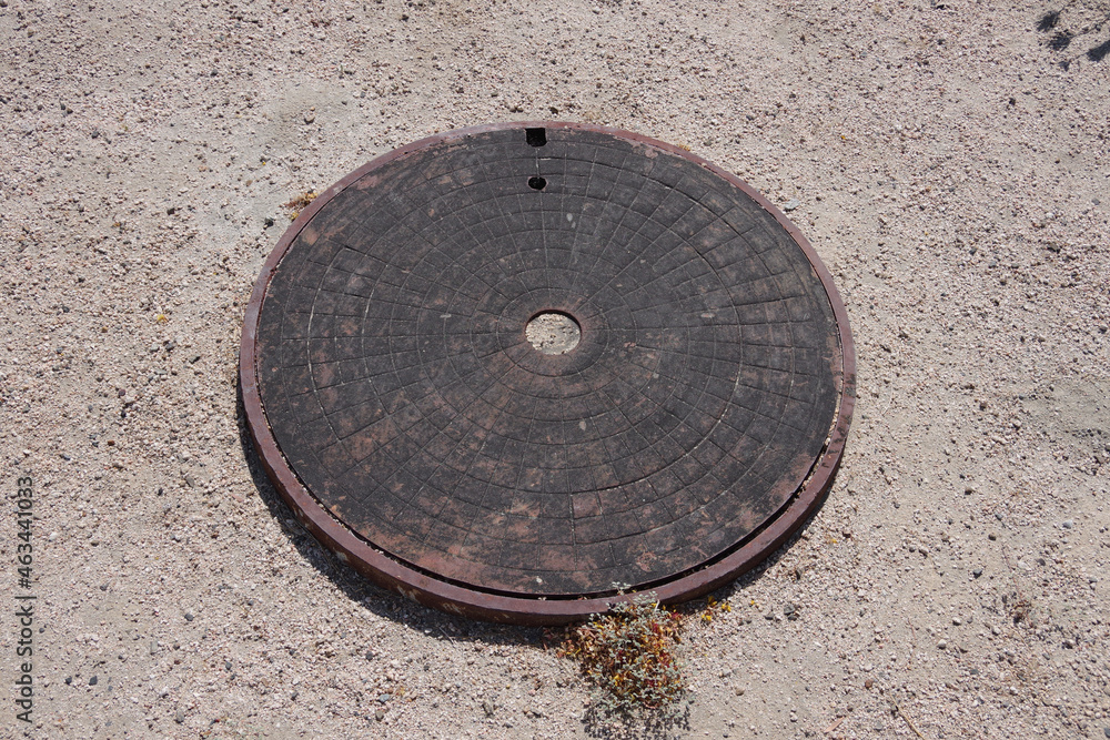 Close-up view of a an iron cover plate for a sewer line on a sandy side road