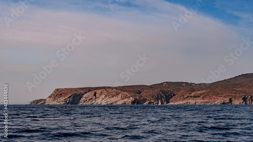 Seaside cliffs and sailboat with Calanans lighthouse next to Cadaques and S'Ocelleta headland, Catalonia, Spain.