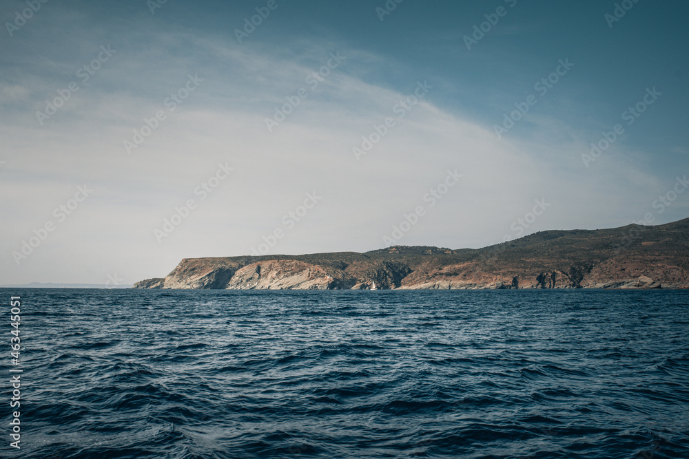 Seaside cliffs and sailboat with Calanans lighthouse next to Cadaques and S'Ocelleta headland, Catalonia, Spain.